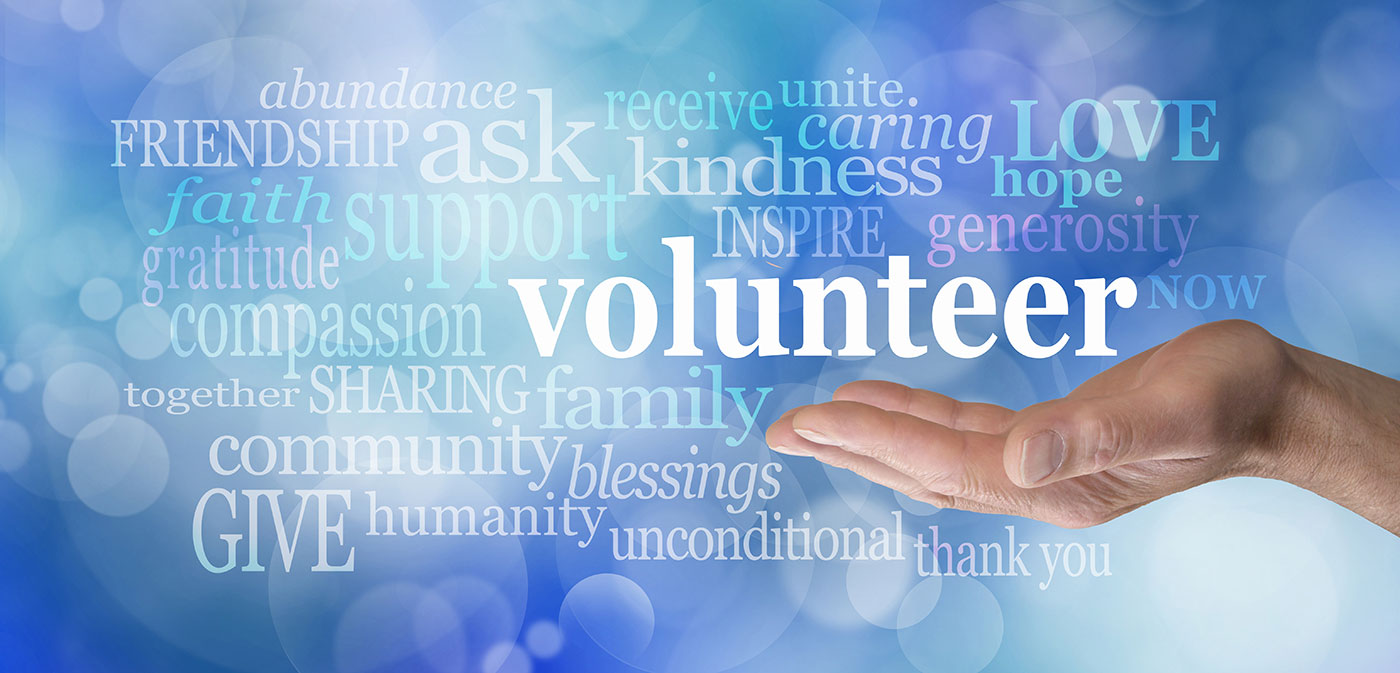 Male hand palm up with the word 'volunteer' floating above surrounded by relevant words on a blue bokeh background